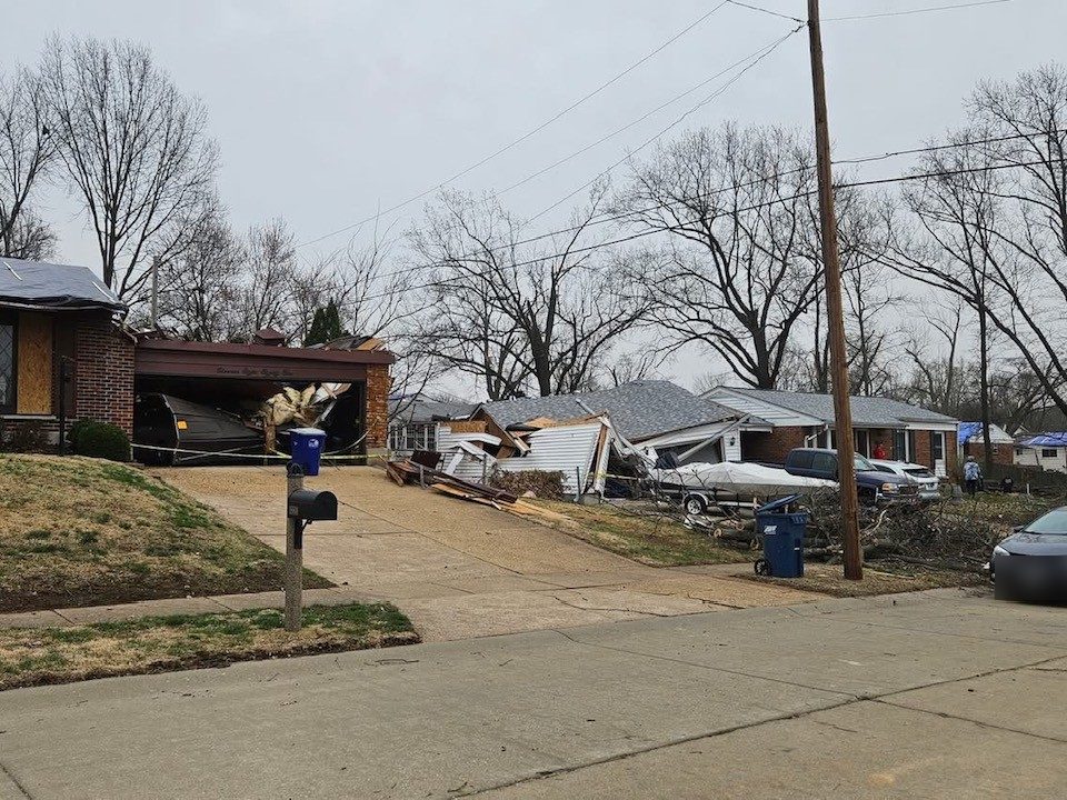 Tornado damage across a residential street, roofs torn open and debris across driveways